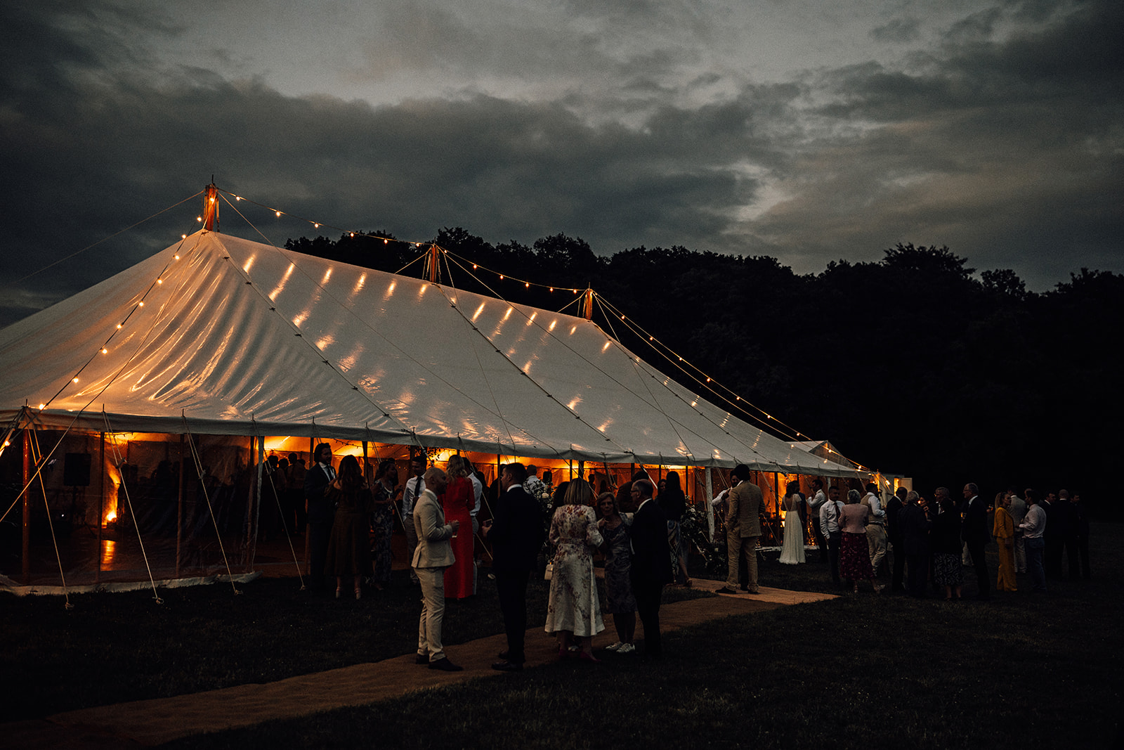 Tilia wedding marquee at dusk with warm golden glow under a stormy sky