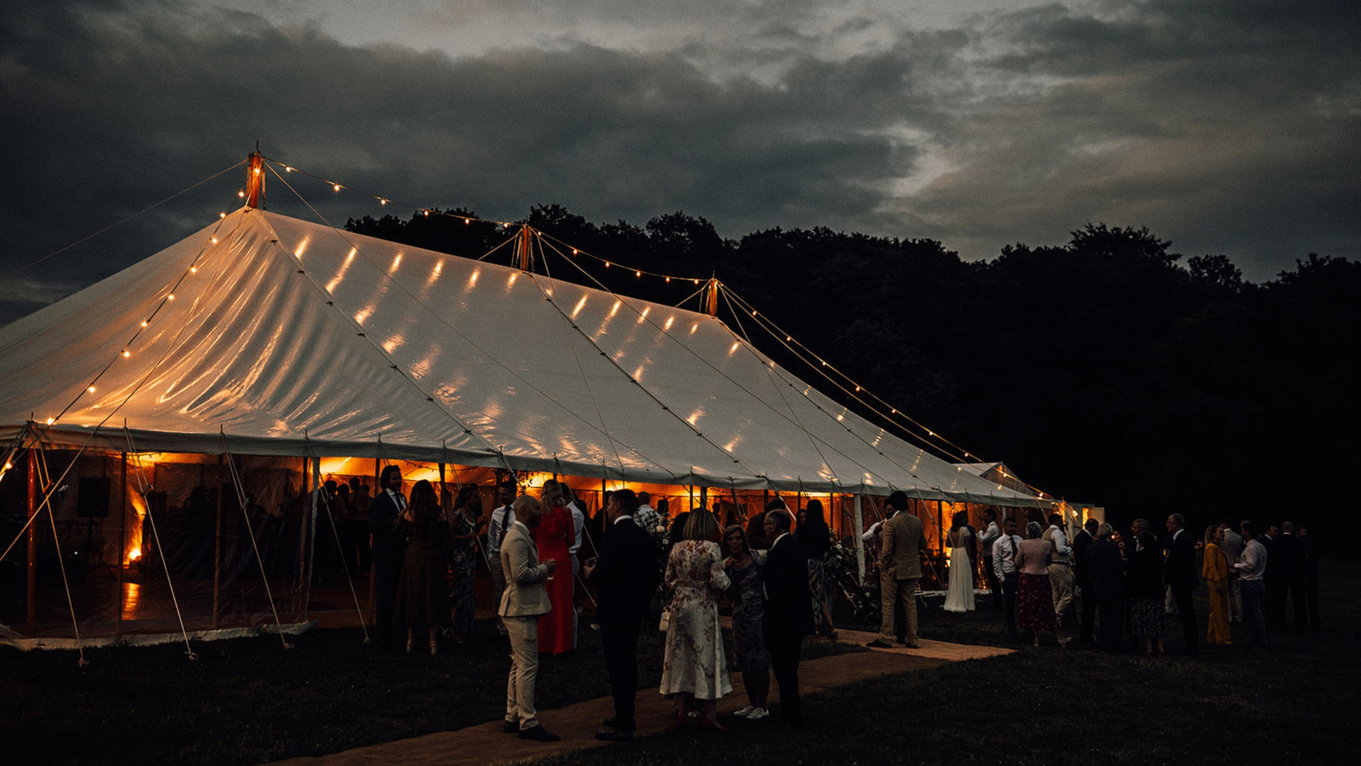 Tilia wedding marquee at dusk with warm golden glow under a stormy sky